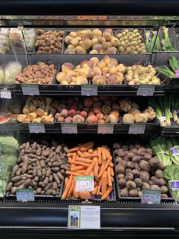 Winter produce on a wet rack at Honest Weight with organic signs on each item